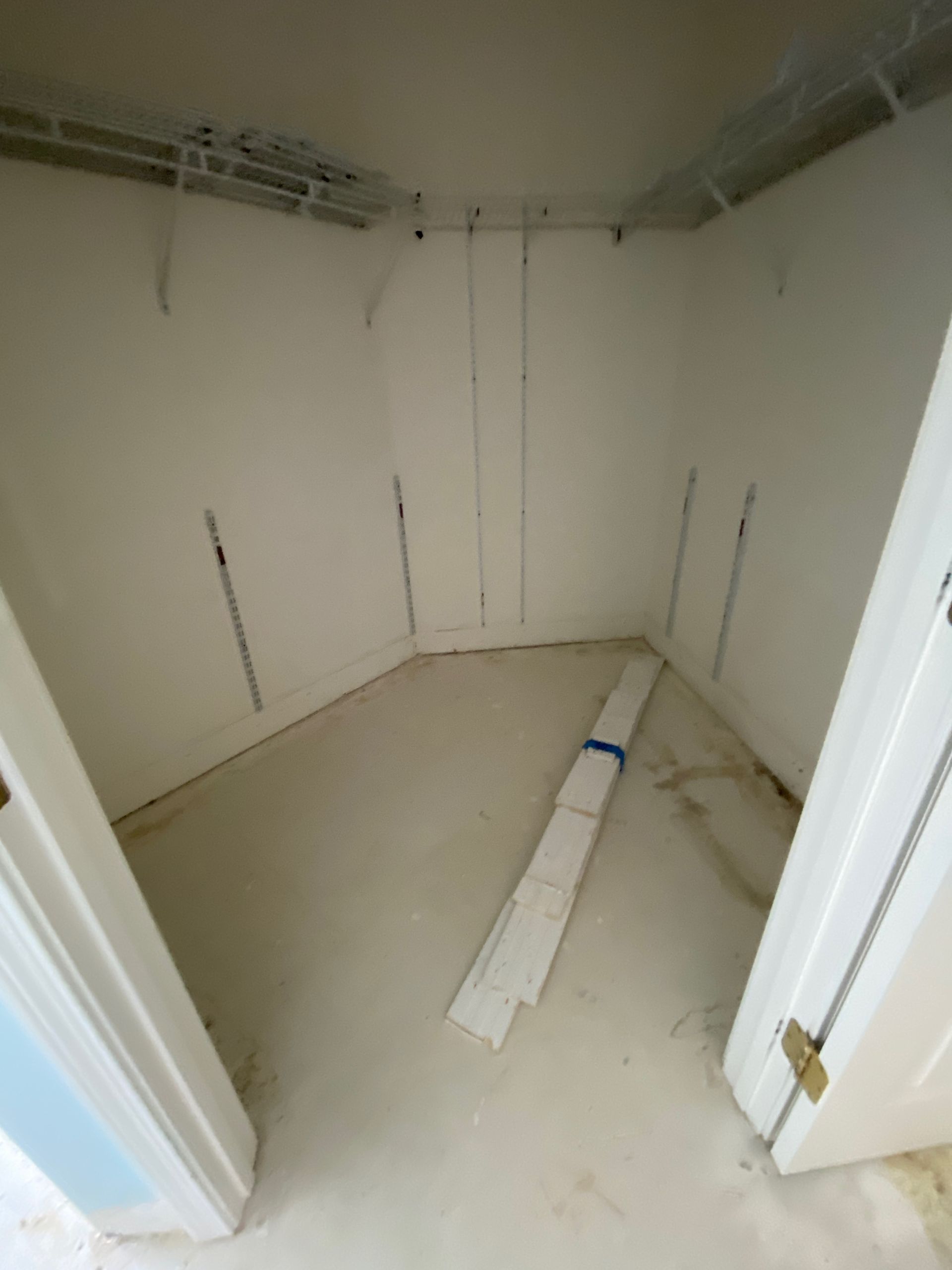 Small unfinished closet with white walls, bare floor, and construction debris on the ground.