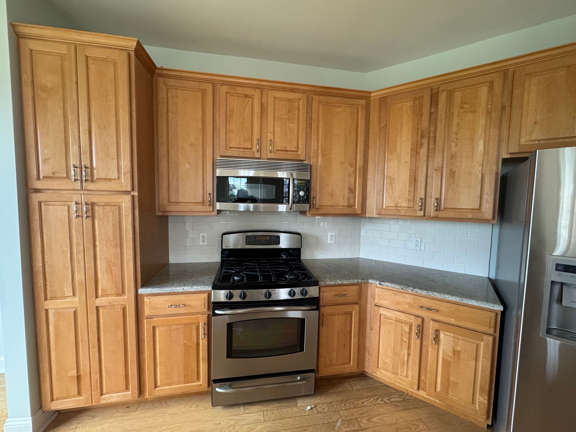 Corner kitchen with light wood cabinets, stainless steel appliances, and gray countertops