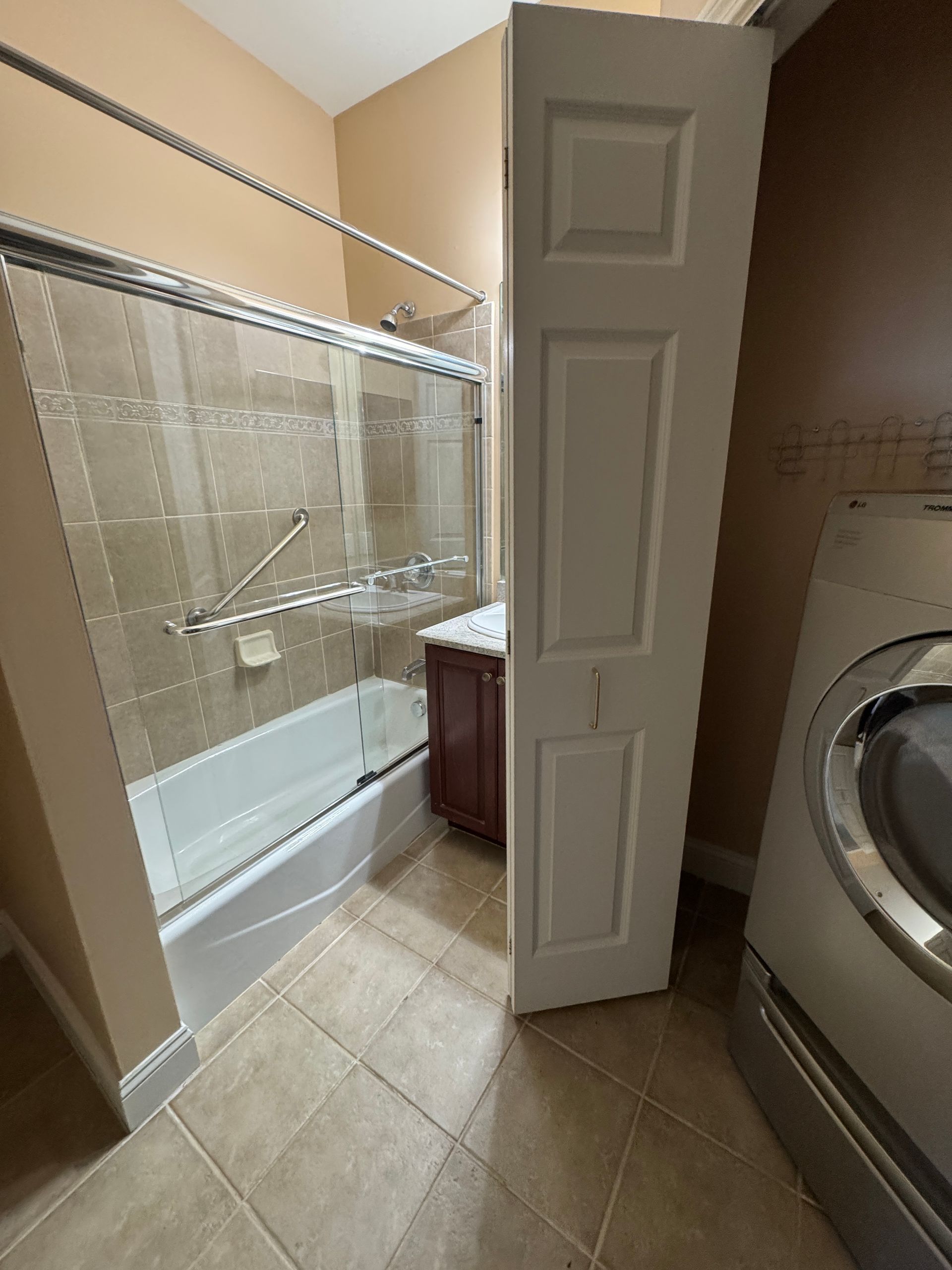 Laundry room with tiled floor, washer, and open door leading to a bathroom shower.