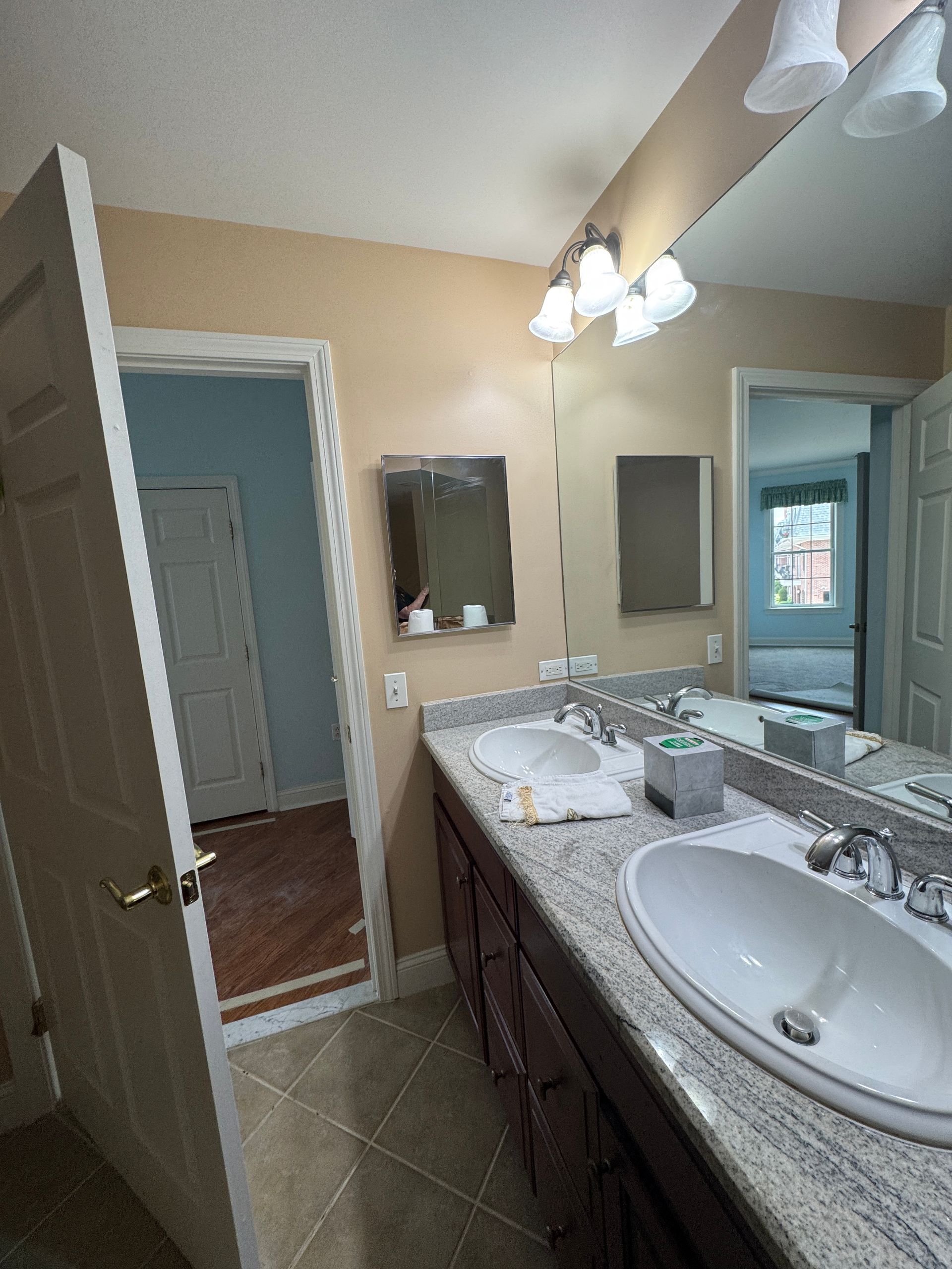 Bathroom with granite double vanity, mirrors, sink, and open doorway to a tiled room.