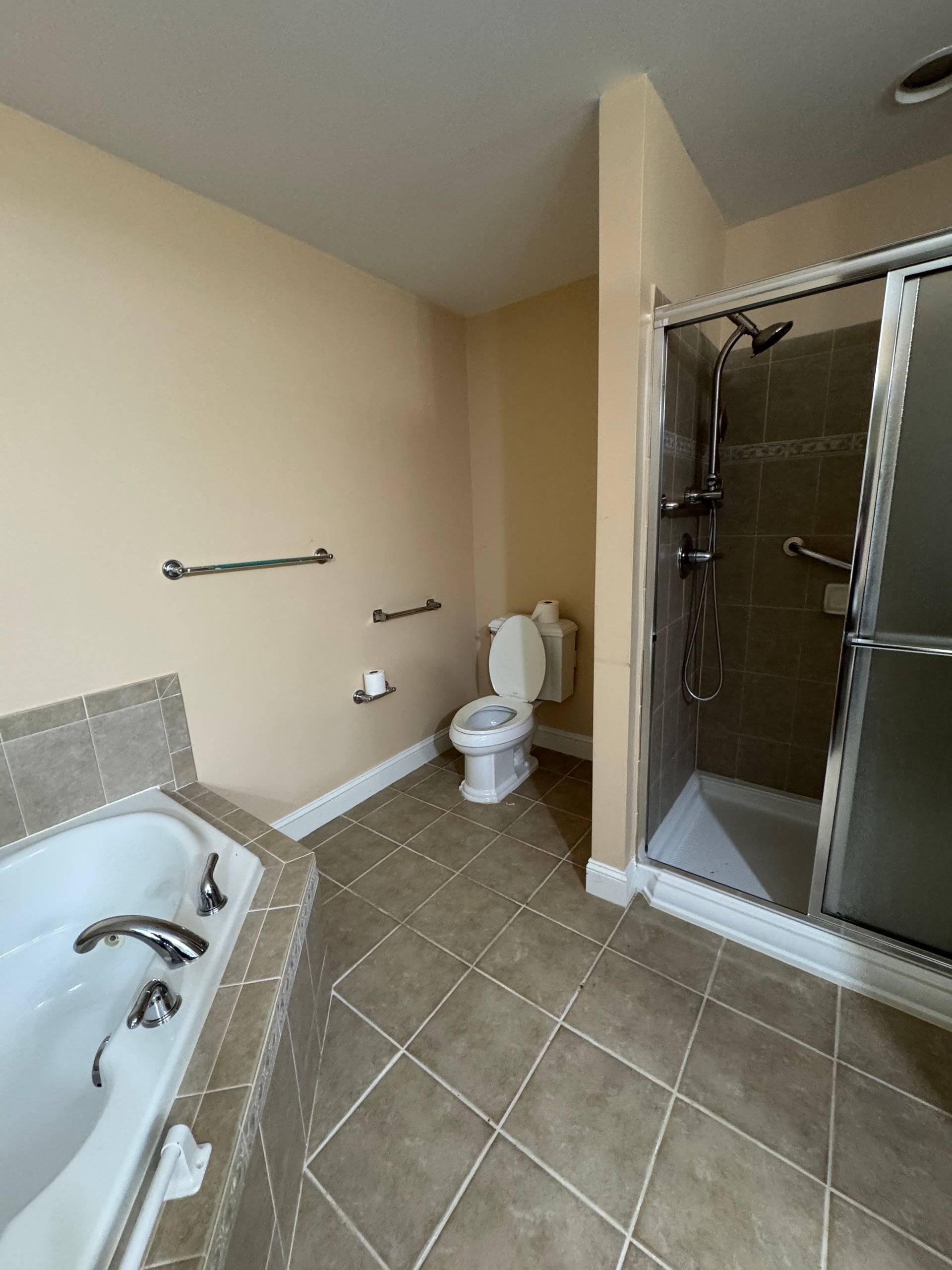 Accessible bathroom with tub, toilet, tiled floor, and glass shower stall.