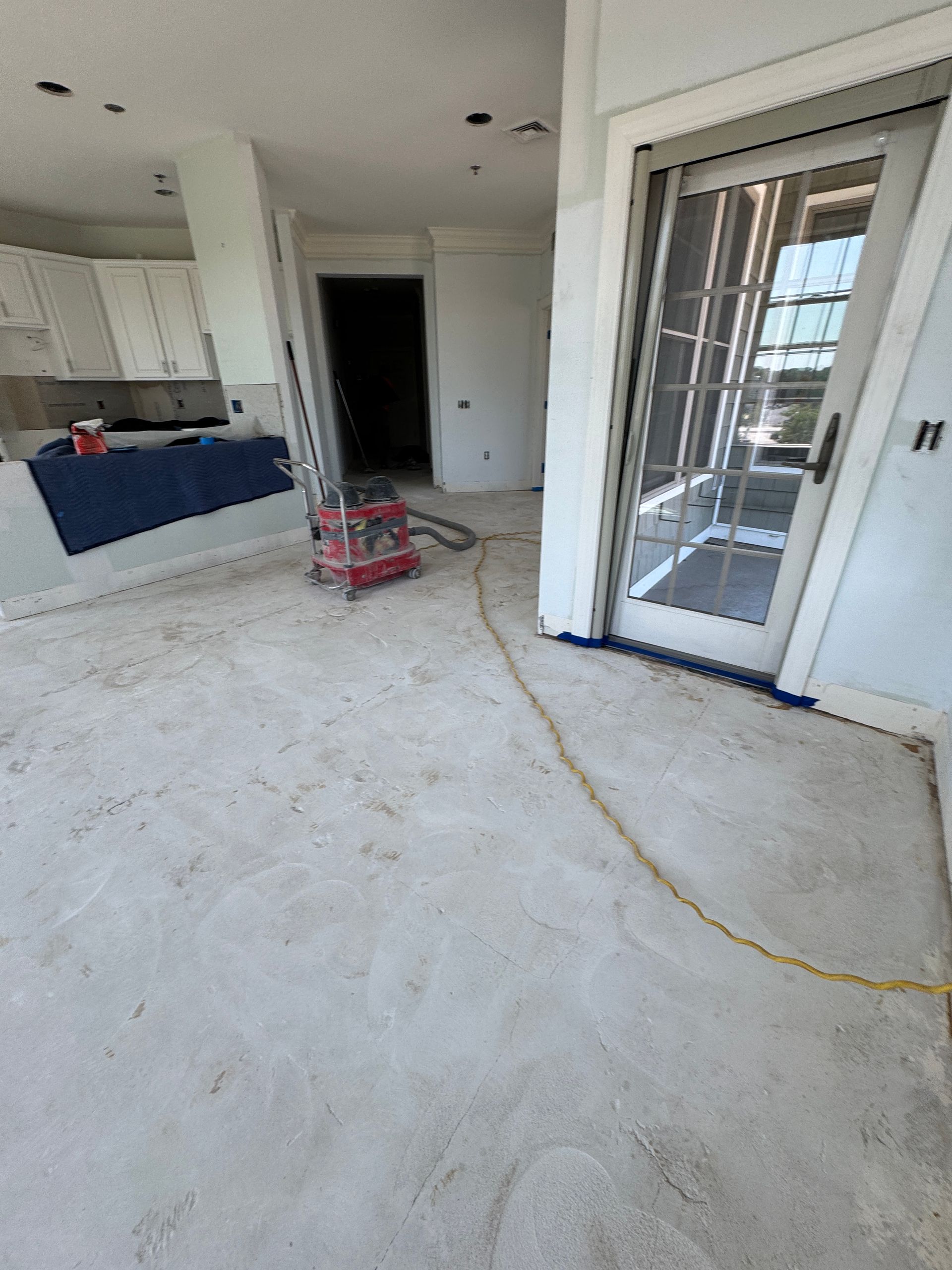 Unfinished kitchen with white cabinets, blue island, and a sliding glass door leading outside.
