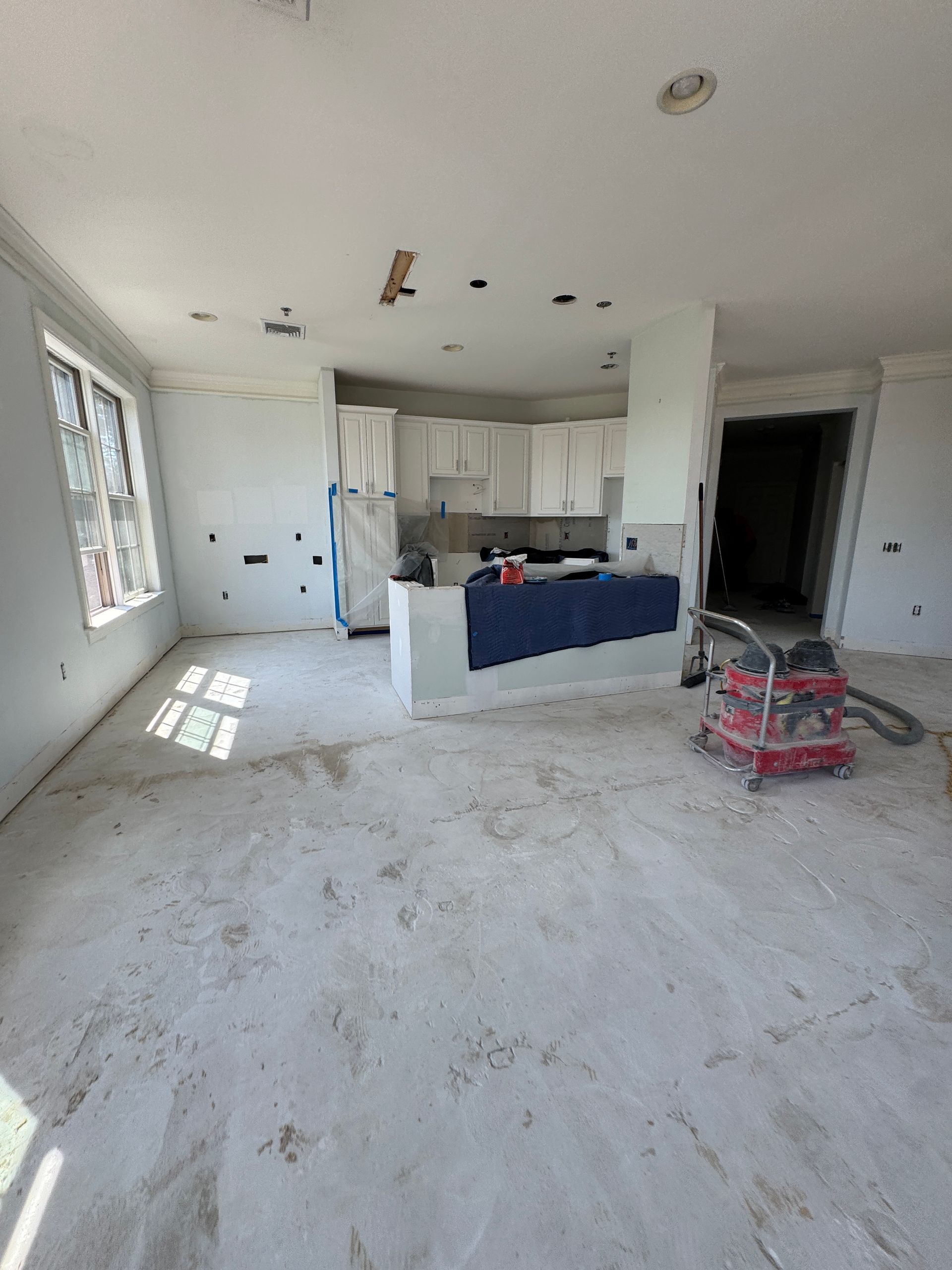 Unfinished kitchen and living area with white cabinets, an island, and construction debris on the floor