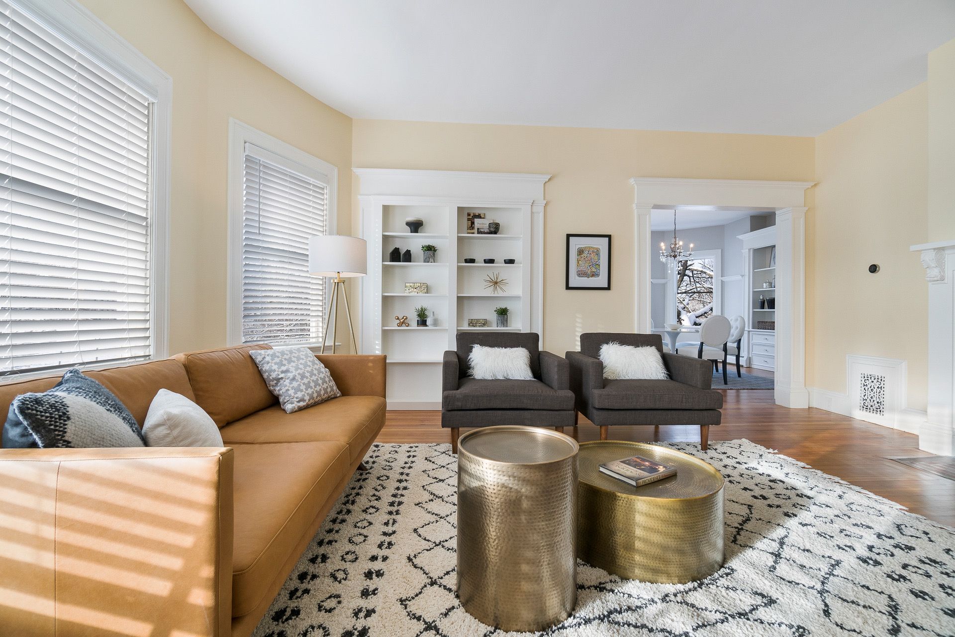 Bright living room with tan sofa, patterned rug, gold tables, and white built-in shelves