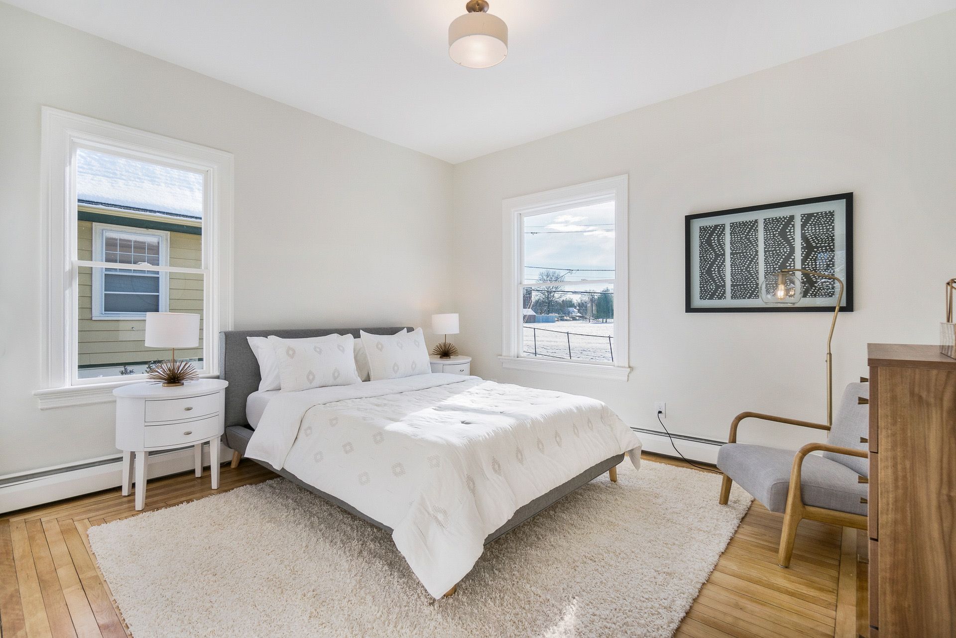 Bright bedroom with a white bed, two windows, a chair, and light wood floors