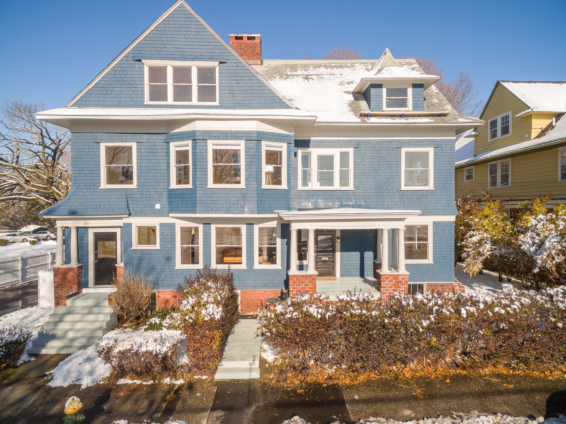 Snow-dusted blue house with white trim and brick steps in a residential neighborhood