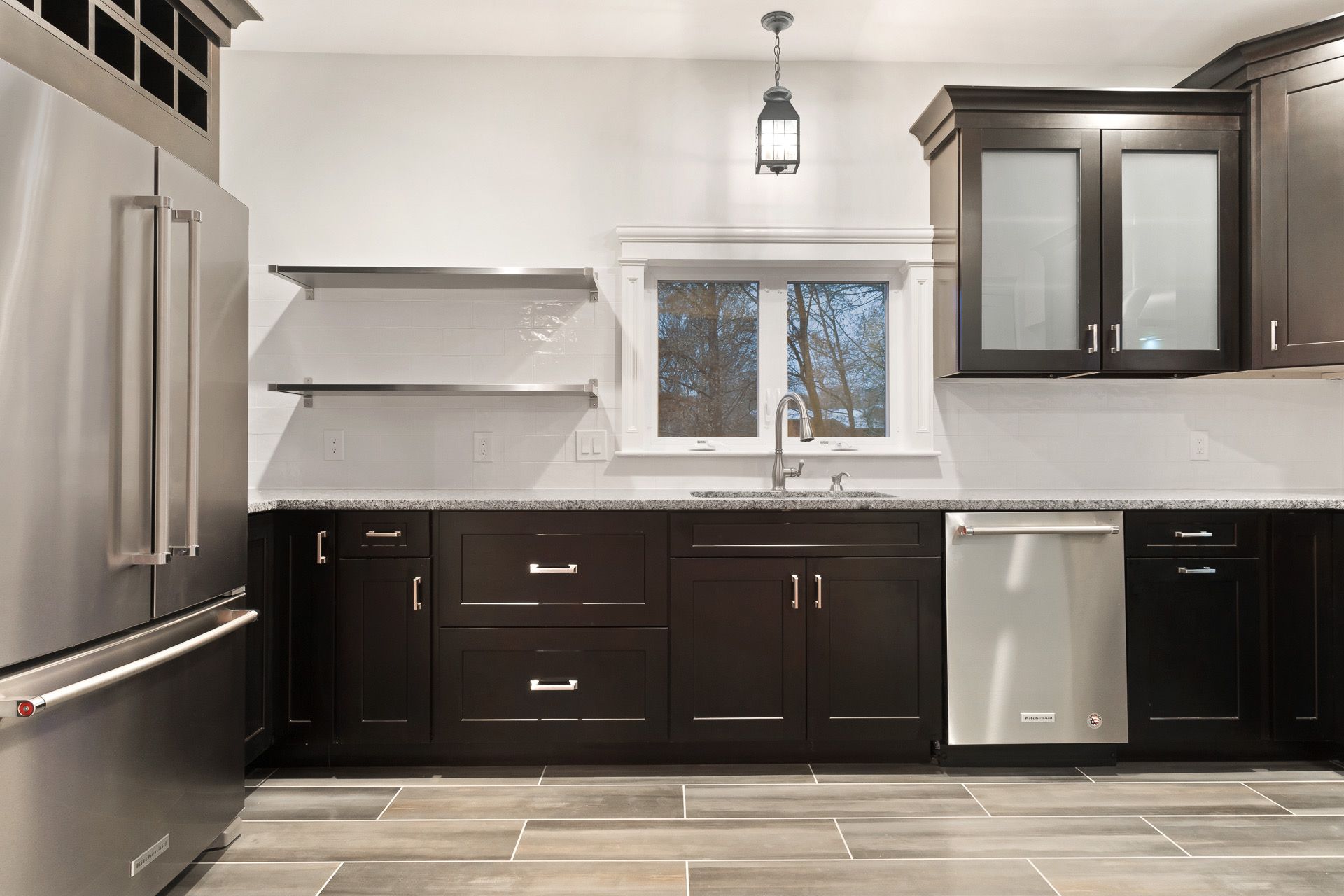 Modern kitchen with dark cabinets, stainless steel appliances, white countertops, and a window above the sink