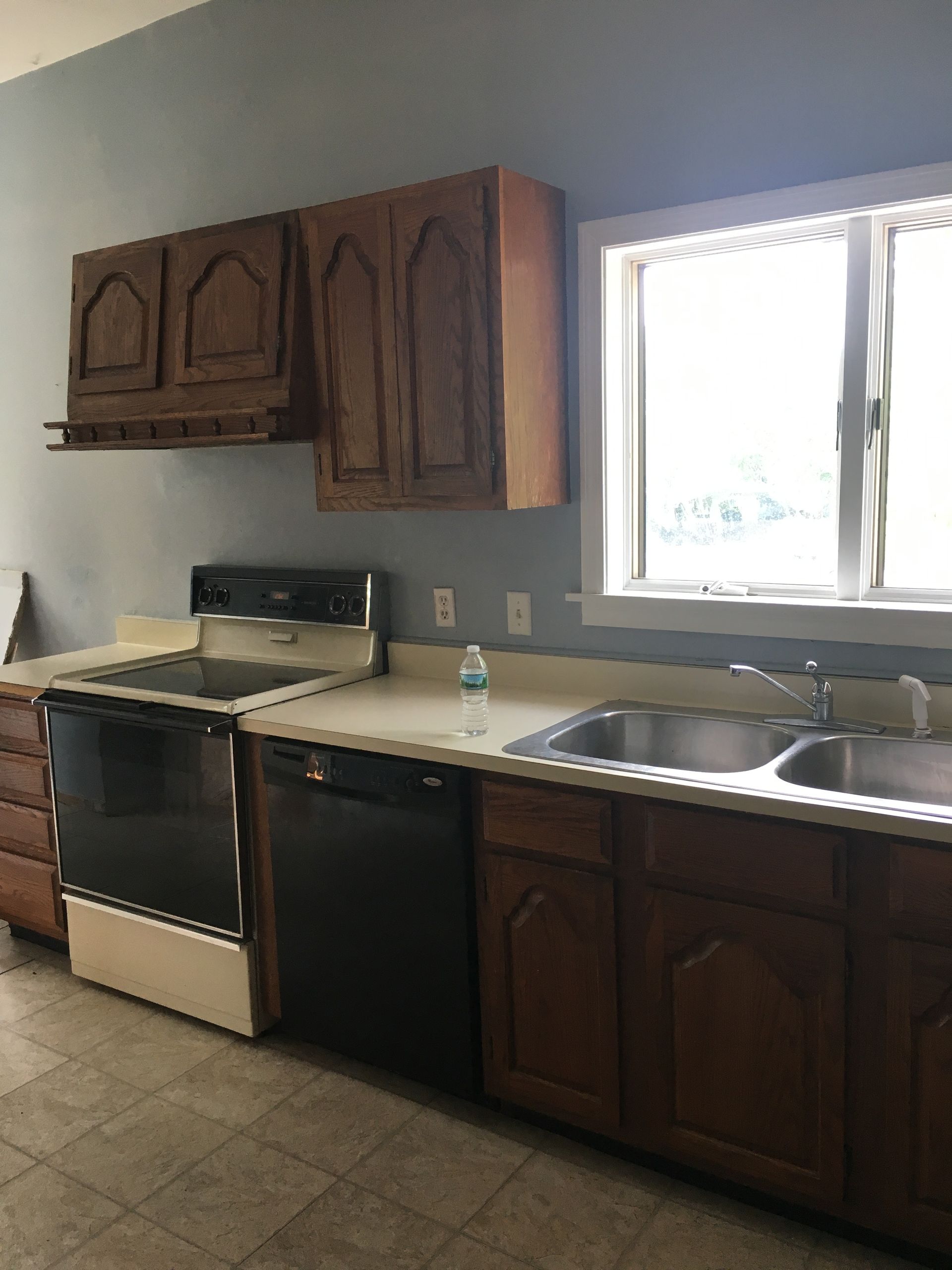 Kitchen with dark wood cabinets, white countertops, stove, sink, and a bright window over the sink.