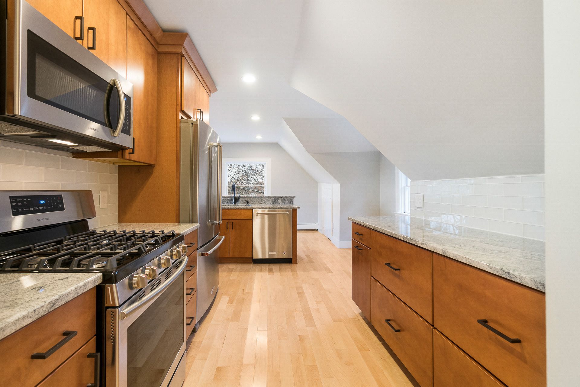Bright, modern kitchen with wood cabinets, a stainless-steel stove, and a long granite countertop.