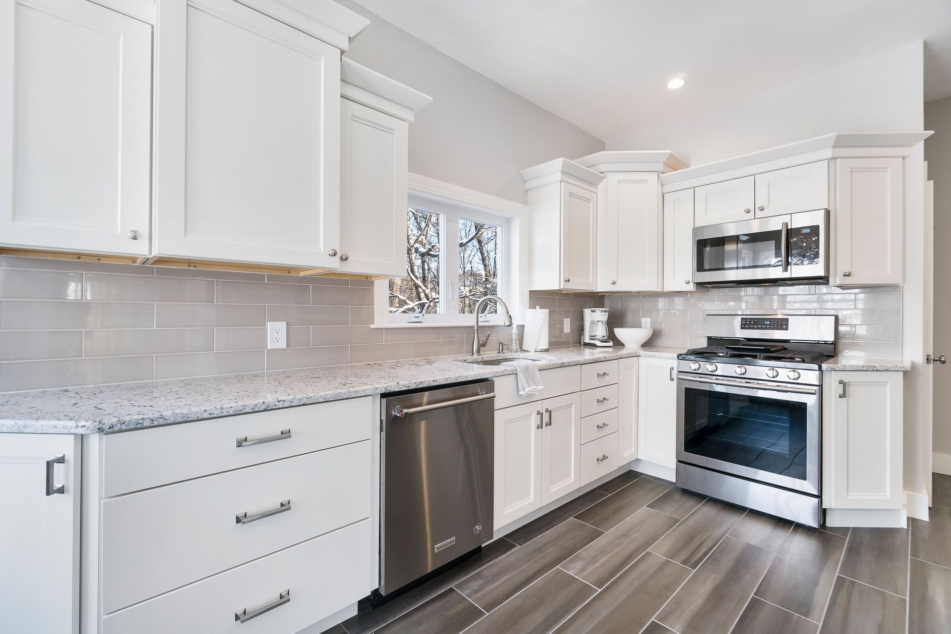 Bright white modern kitchen with white cabinets, stainless appliances, and gray wood floors