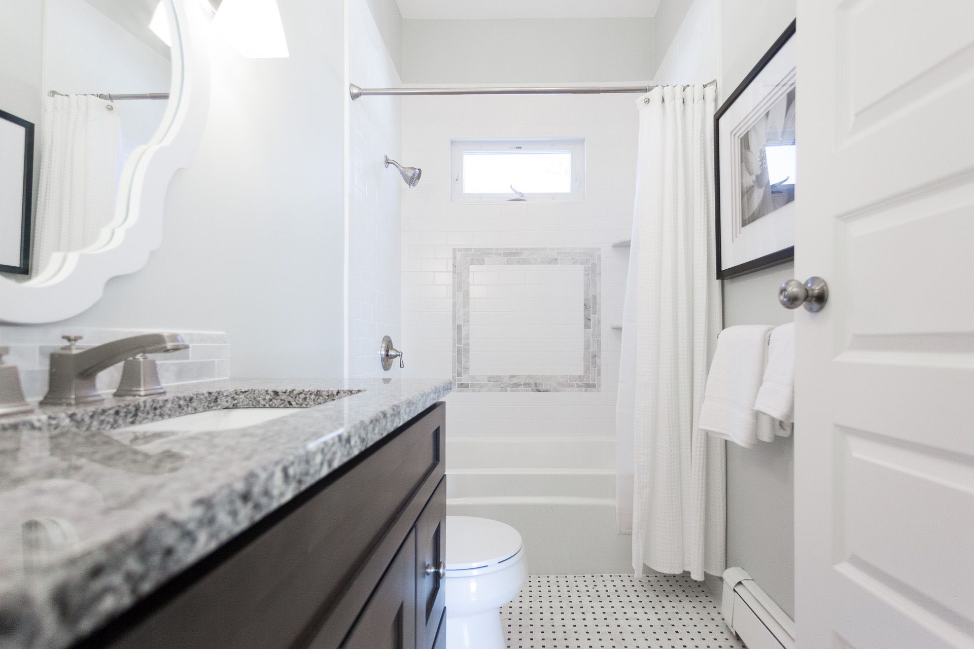Bright white bathroom with dark vanity, granite countertop, toilet, shower, and small window