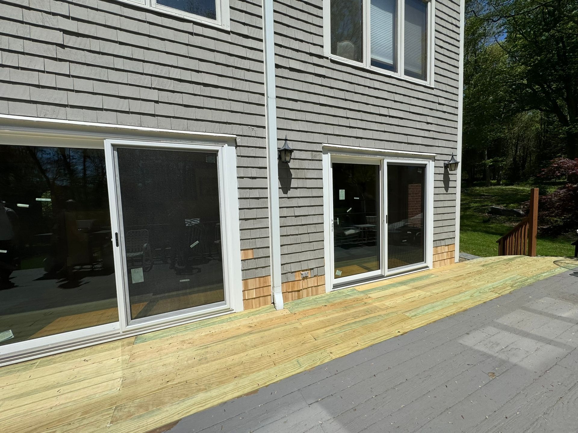 Exterior of a gray house with large sliding glass doors and a newly built wooden deck beside a paved driveway