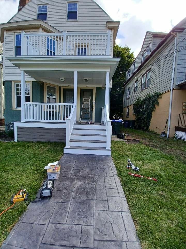 Front view of a gray house with a porch, stairs, and concrete walkway under construction.