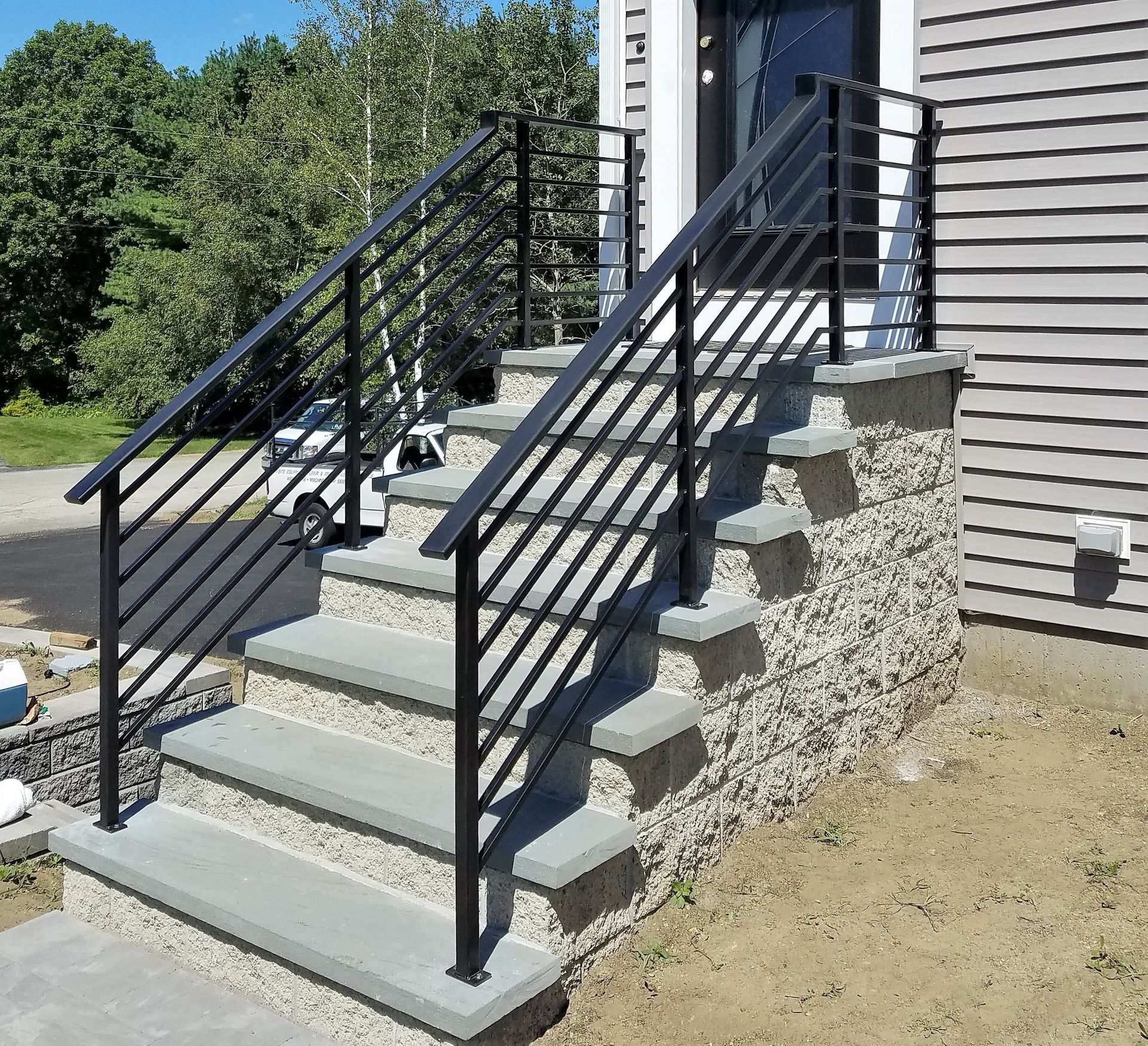 Concrete outdoor stairs with black metal railings beside a house on a sunny day