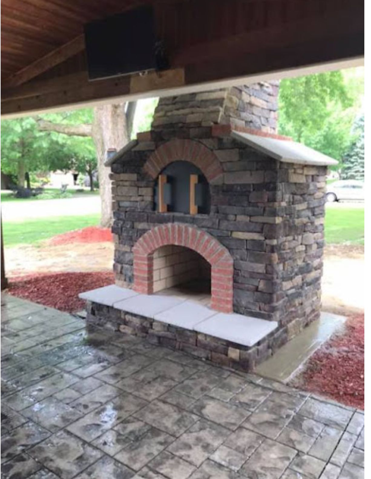 Outdoor brick pizza oven under a pavilion, with arched openings and a white stone shelf.