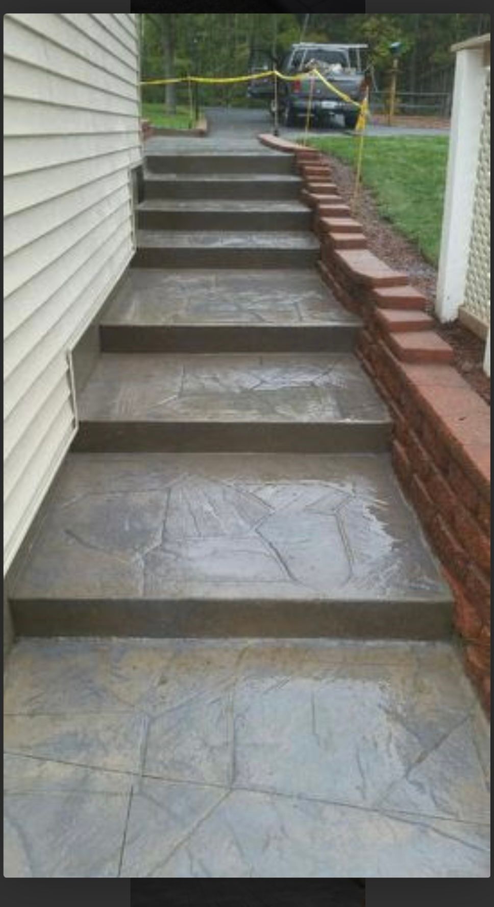 Concrete front steps with tiled landing and brick side wall leading to a yard.