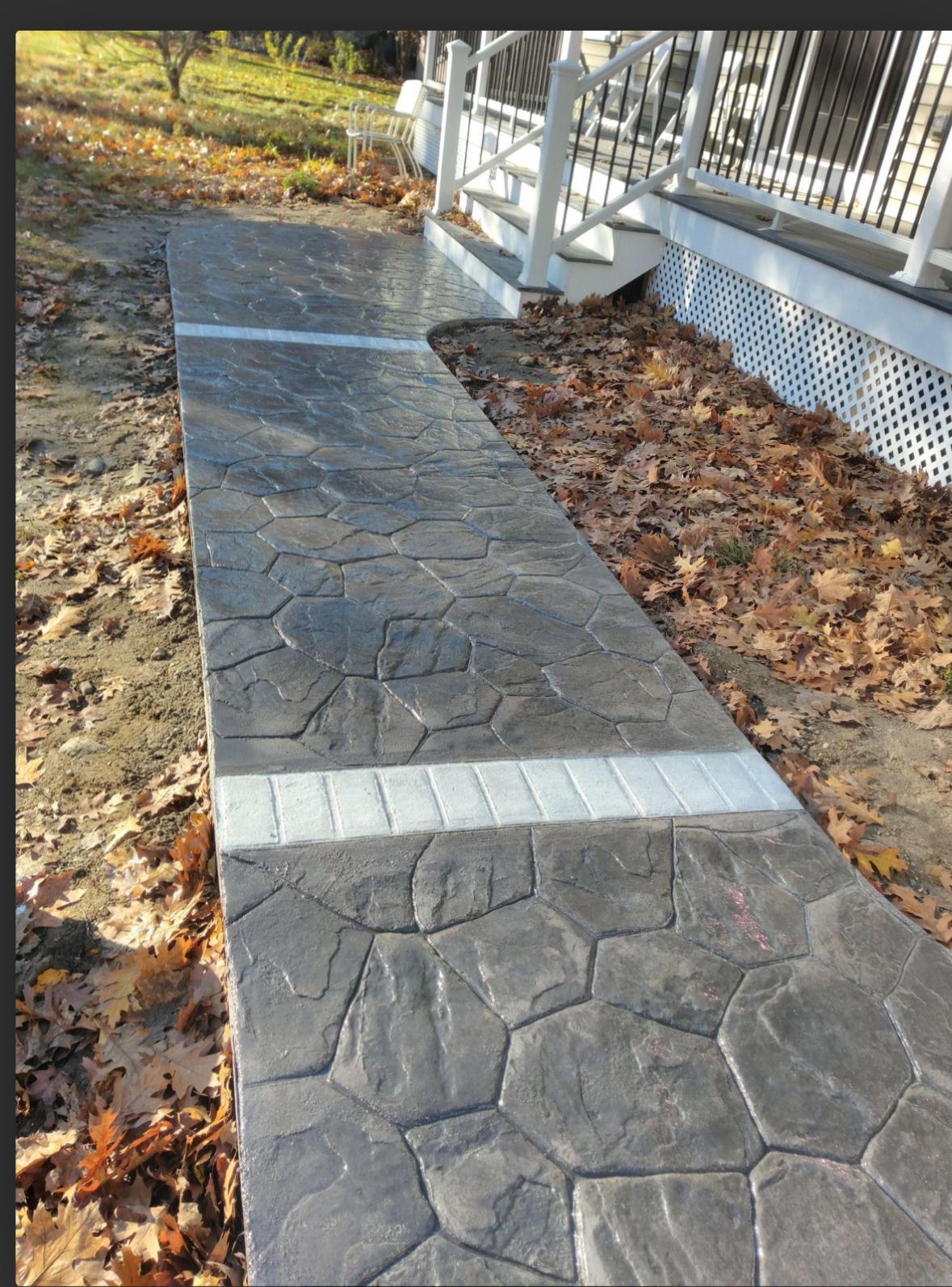 Stone-look walkway with white ramps leading to a porch beside fallen autumn leaves.