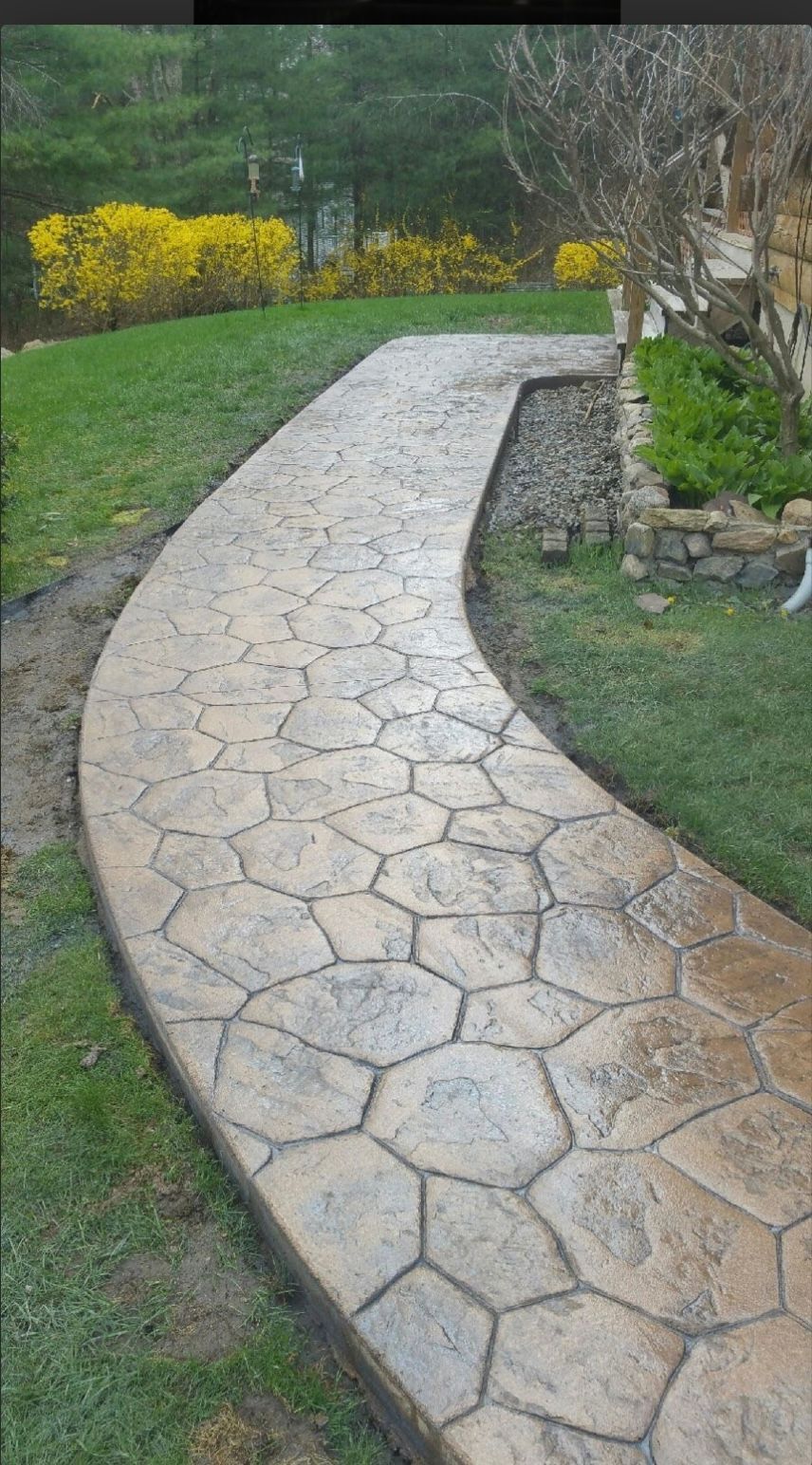 Curved stone walkway through a green garden with yellow shrubs and a rock border