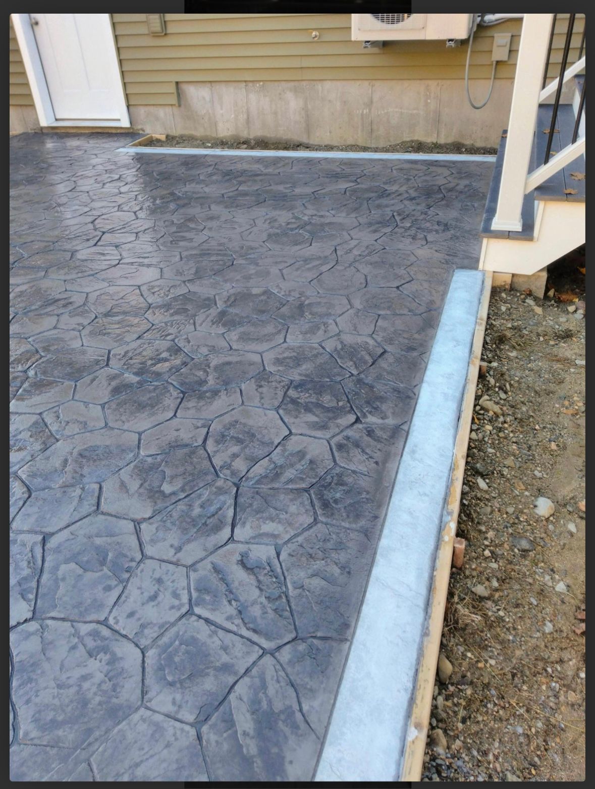 Stamped concrete patio beside a house, bordered by a light blue curb and gravel edge