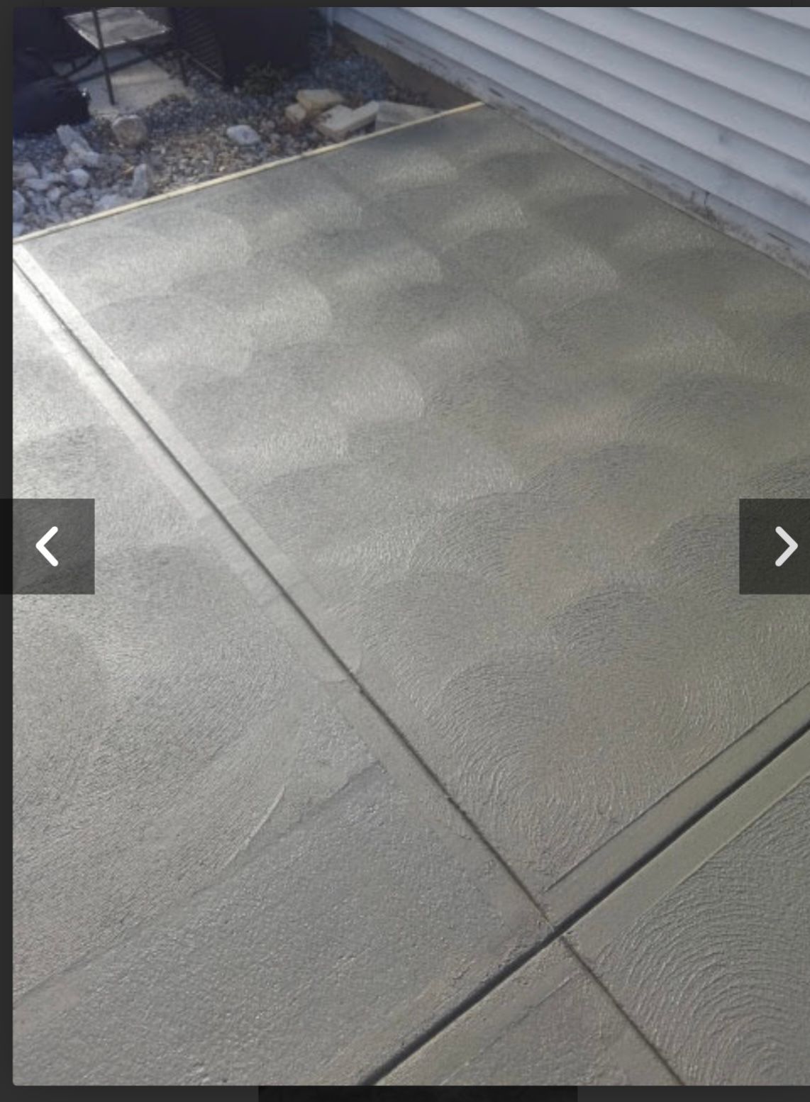 Gray textured concrete patio beside a house with siding and a small gravel border