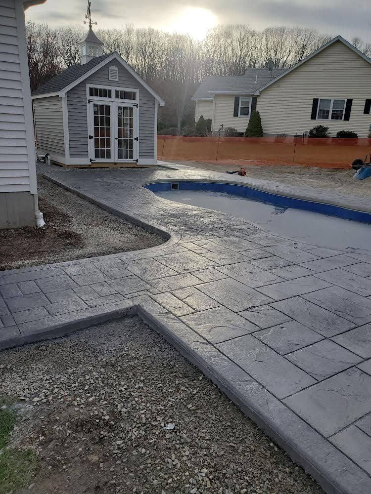 Backyard patio with pavers, a small shed, gravel border, and a fenced pool in winter light