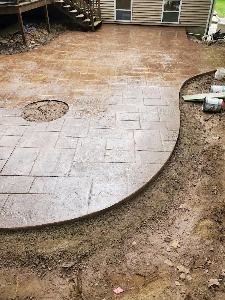 Freshly stamped concrete patio beside a house, with curved edge and exposed dirt border