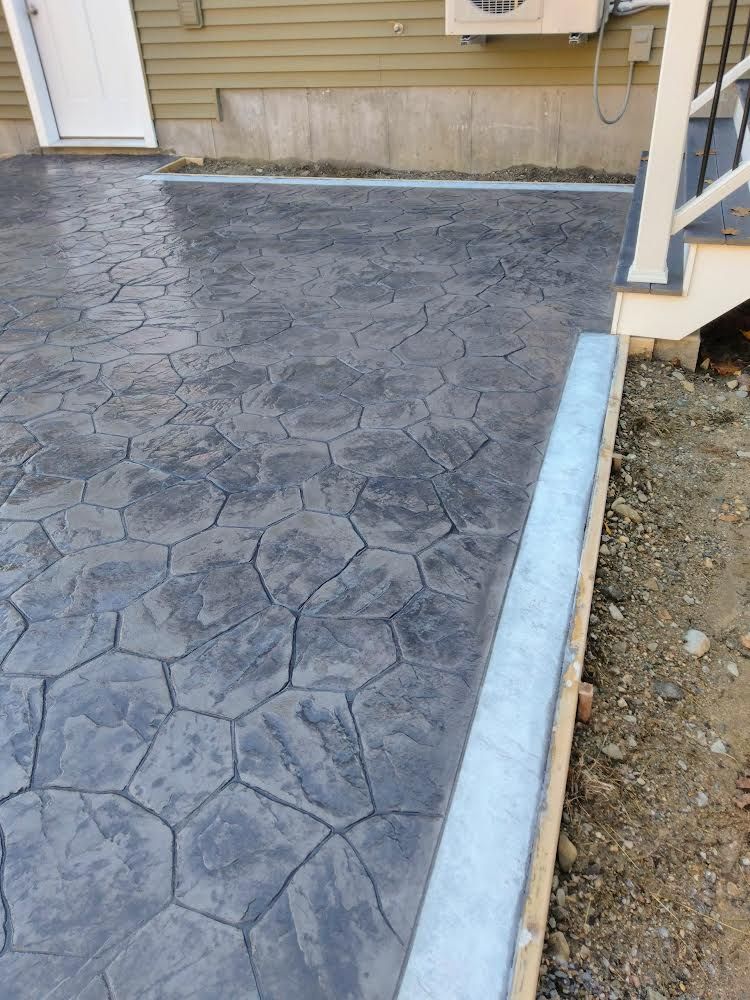 Stamped concrete driveway beside a house, with a blue curb edge and gravel strip on the right