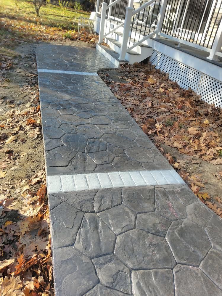 Stamped concrete walkway beside a white porch, with autumn leaves along the edges.
