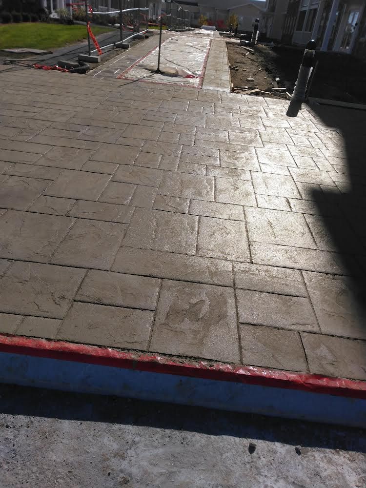 Paved walkway with a ramp under construction, bordered by orange cones and construction barriers.