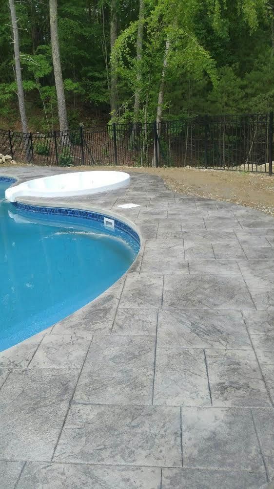 Backyard pool with gray stone patio, white lounge chair, and trees in the background