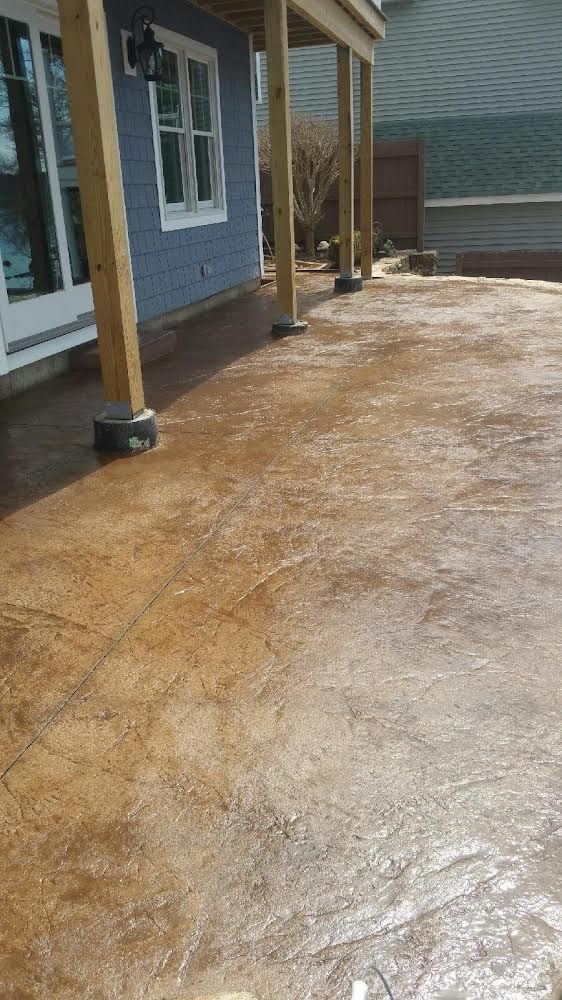 Freshly poured concrete walkway beside a blue house with wooden posts and wet surface.