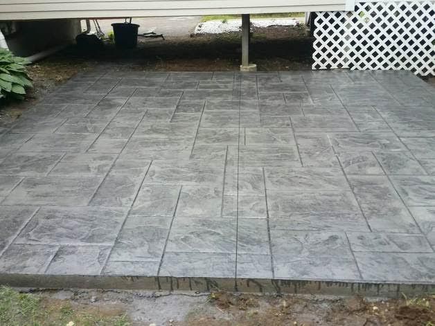 Gray stamped concrete patio in front of a house, with a white lattice skirt on the right.