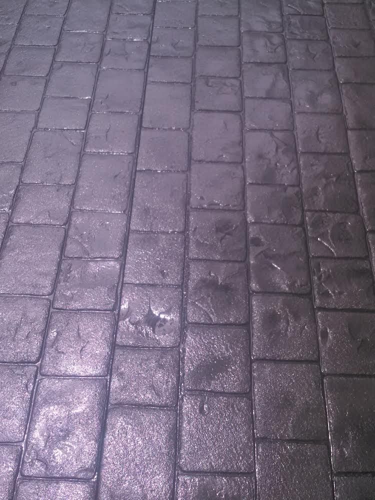 Wet purple-gray brick pavement with puddles and a reflective sheen