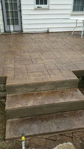 Concrete patio and three steps leading to a white house with windows and a small chair on the right.