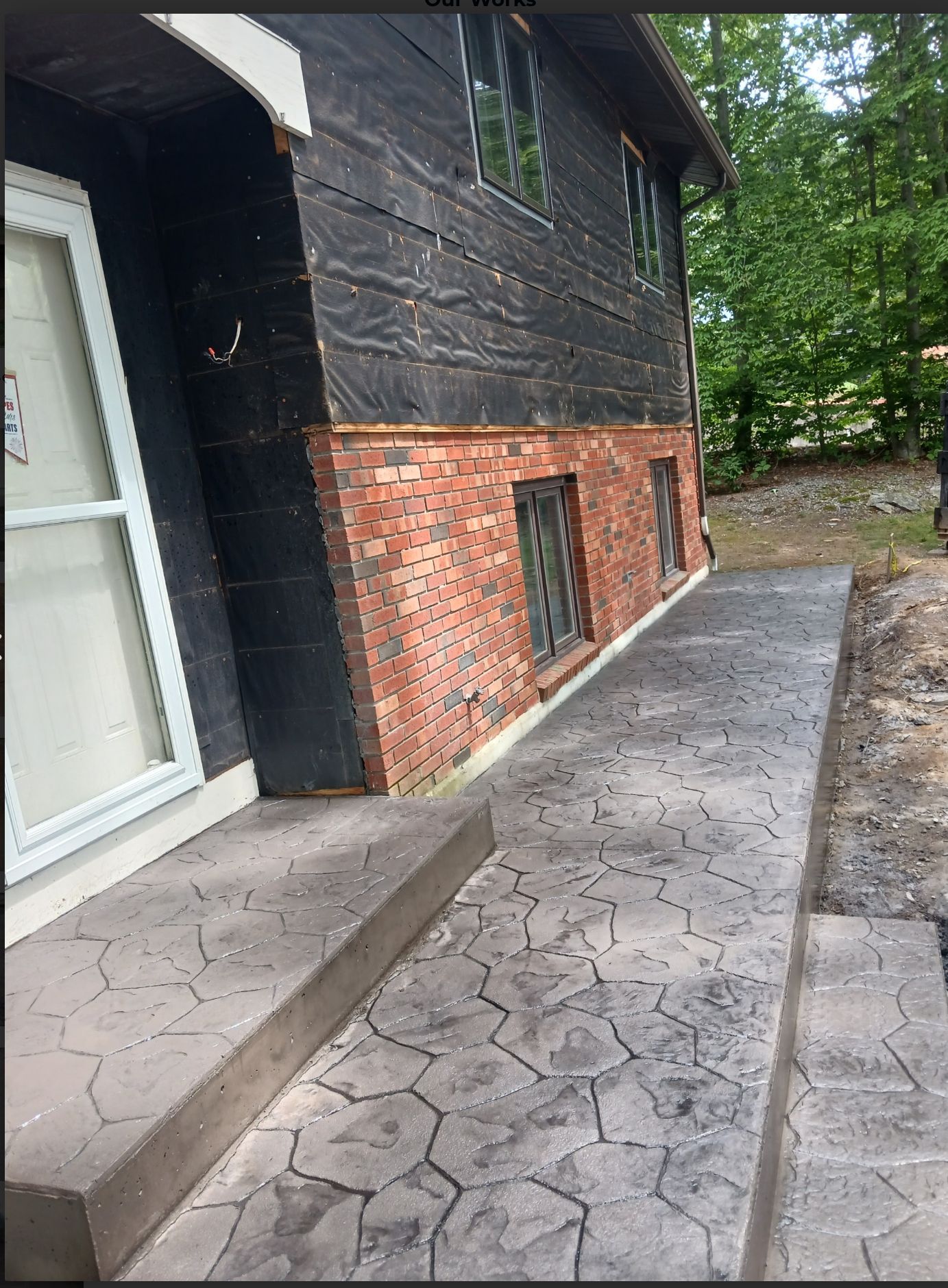 Side of house with brick foundation and cracked concrete walkway beside a white door.