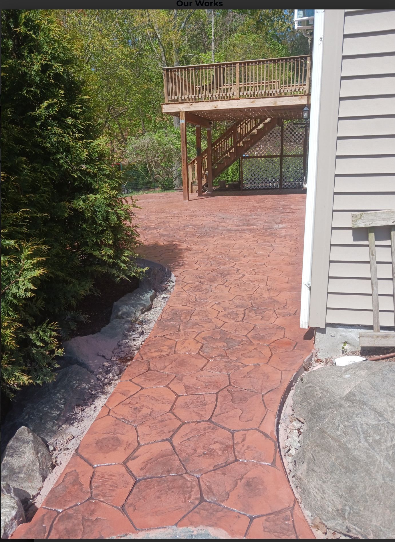 Stone walkway leading to a wooden deck beside a house and trees