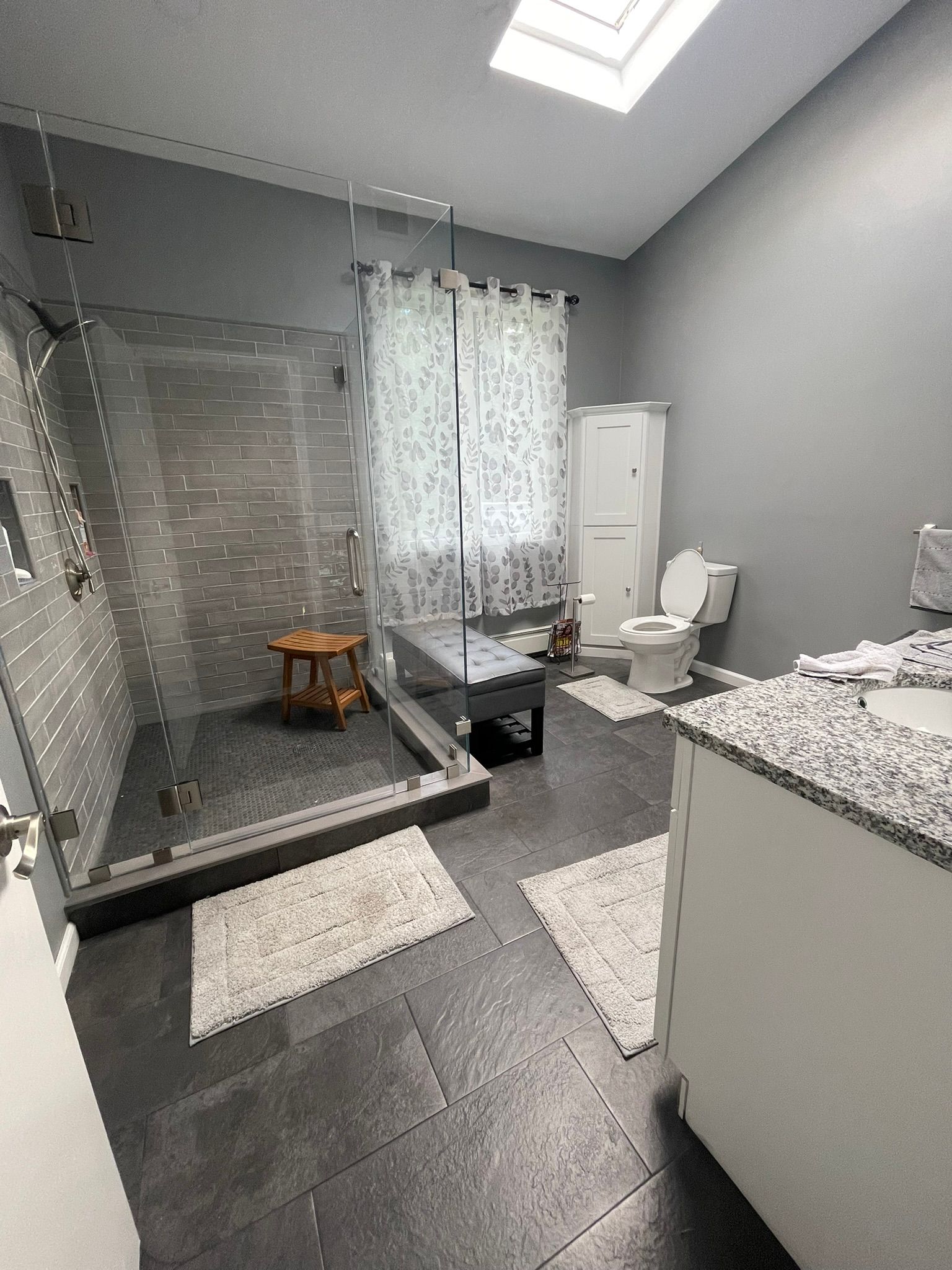 Modern gray bathroom with glass shower, toilet, vanity, and skylight