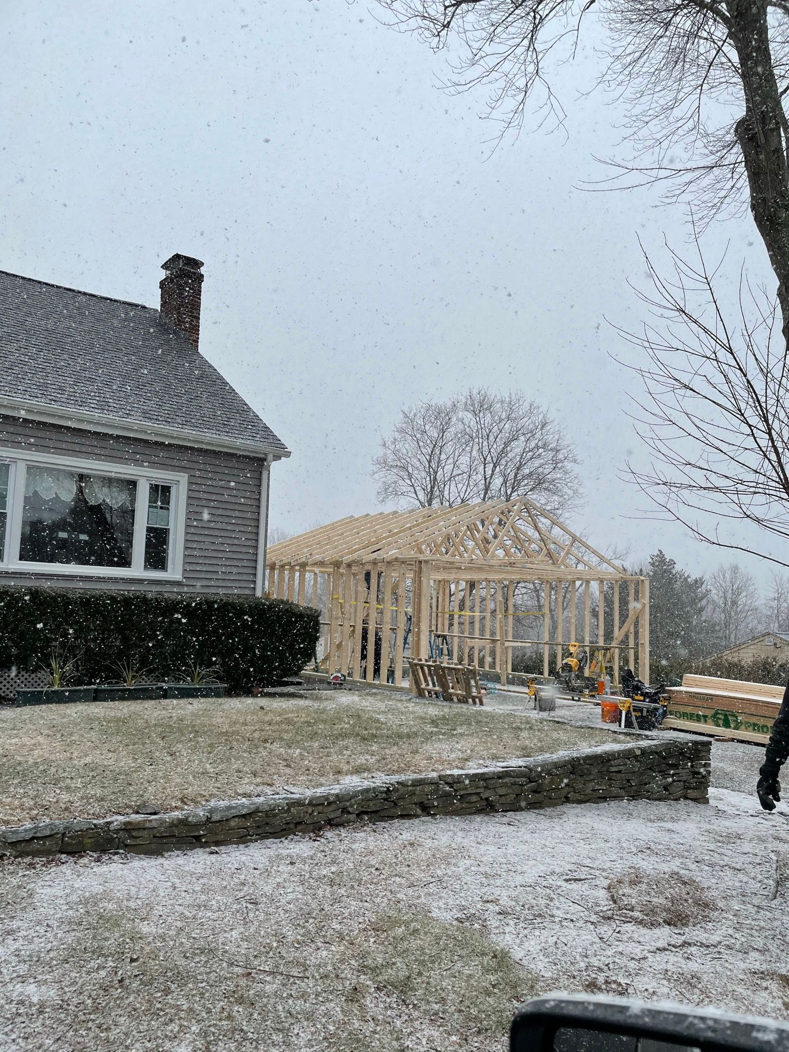Snowy suburban yard with a house and a partially built wooden structure in the background