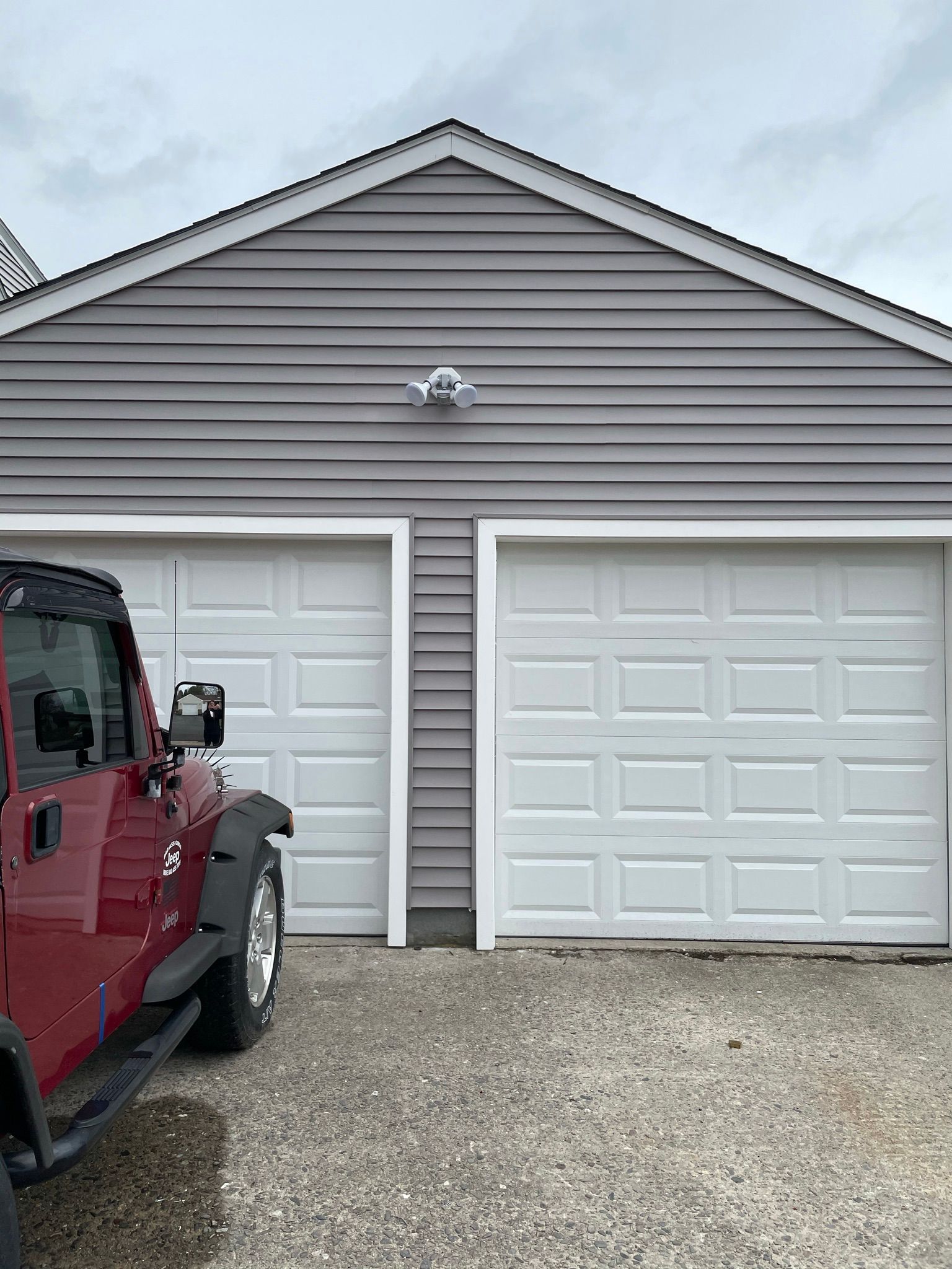 Two-car garage with gray siding and white doors, red Jeep parked on the left.