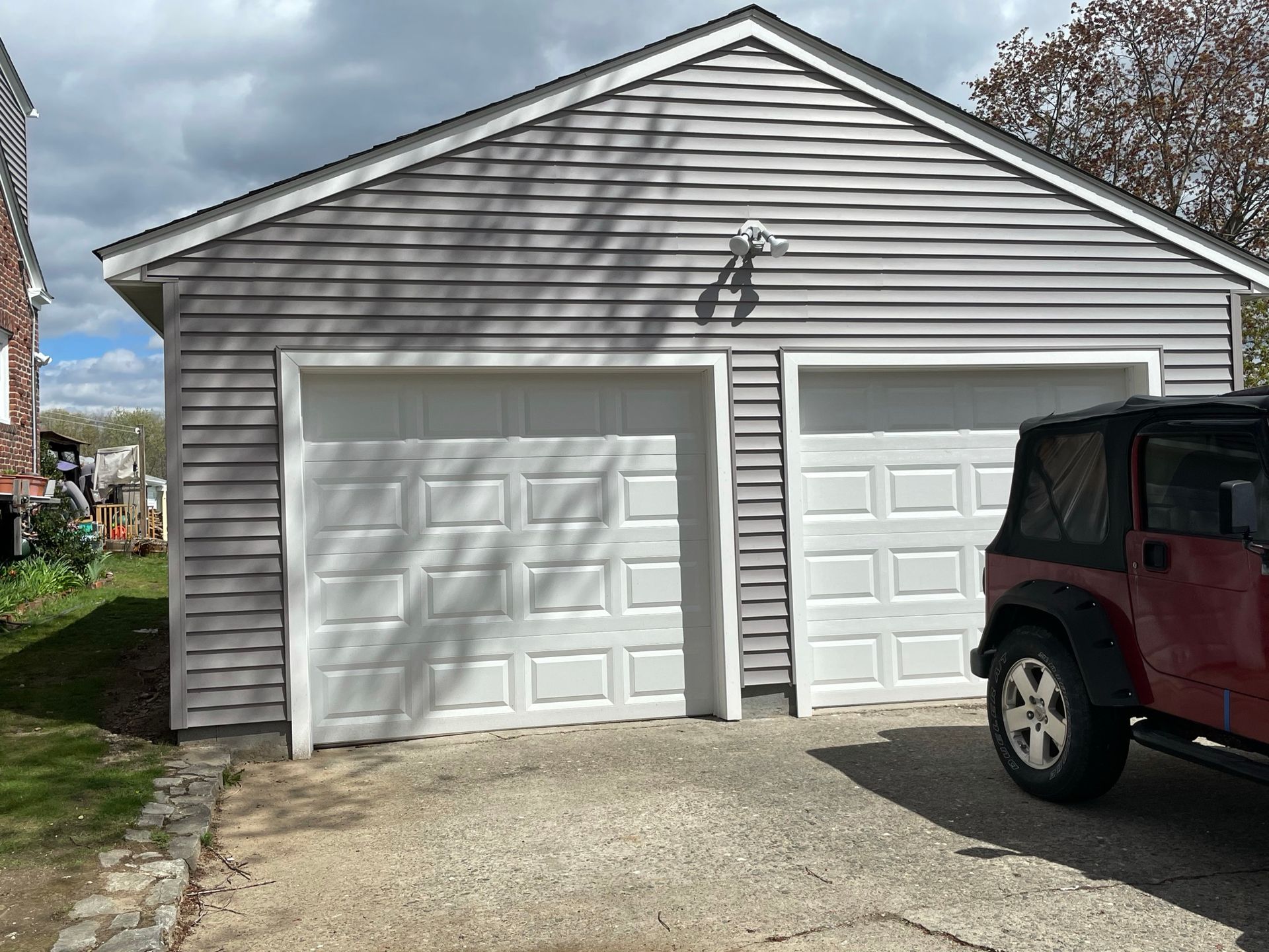 Two-car garage with gray siding and white doors; a red SUV is parked on the right.