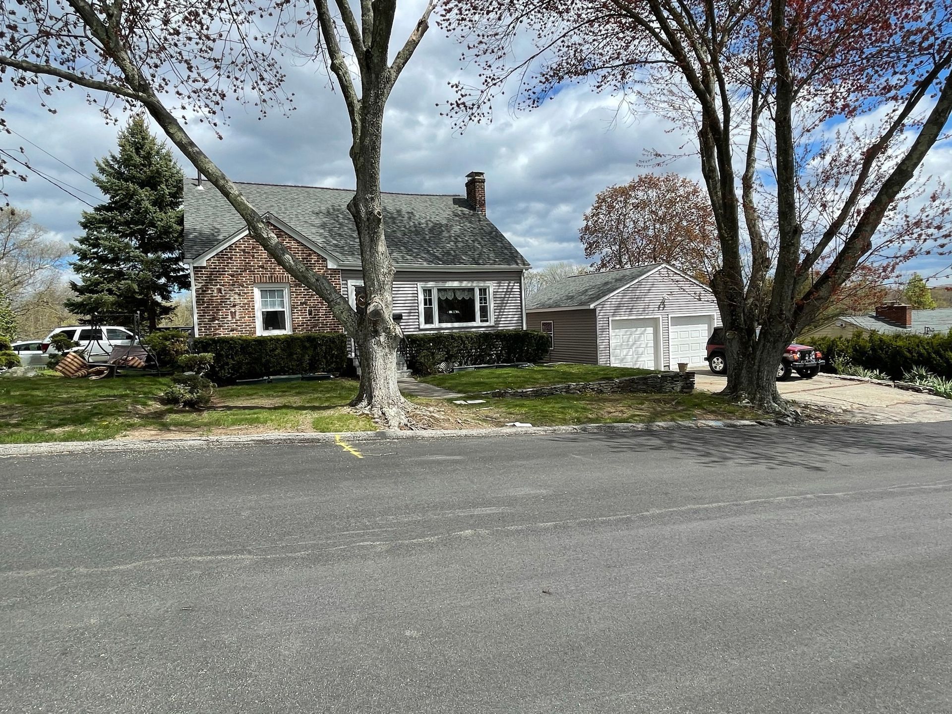 Suburban house with stone facade and white garage under cloudy skies, seen from across the road.