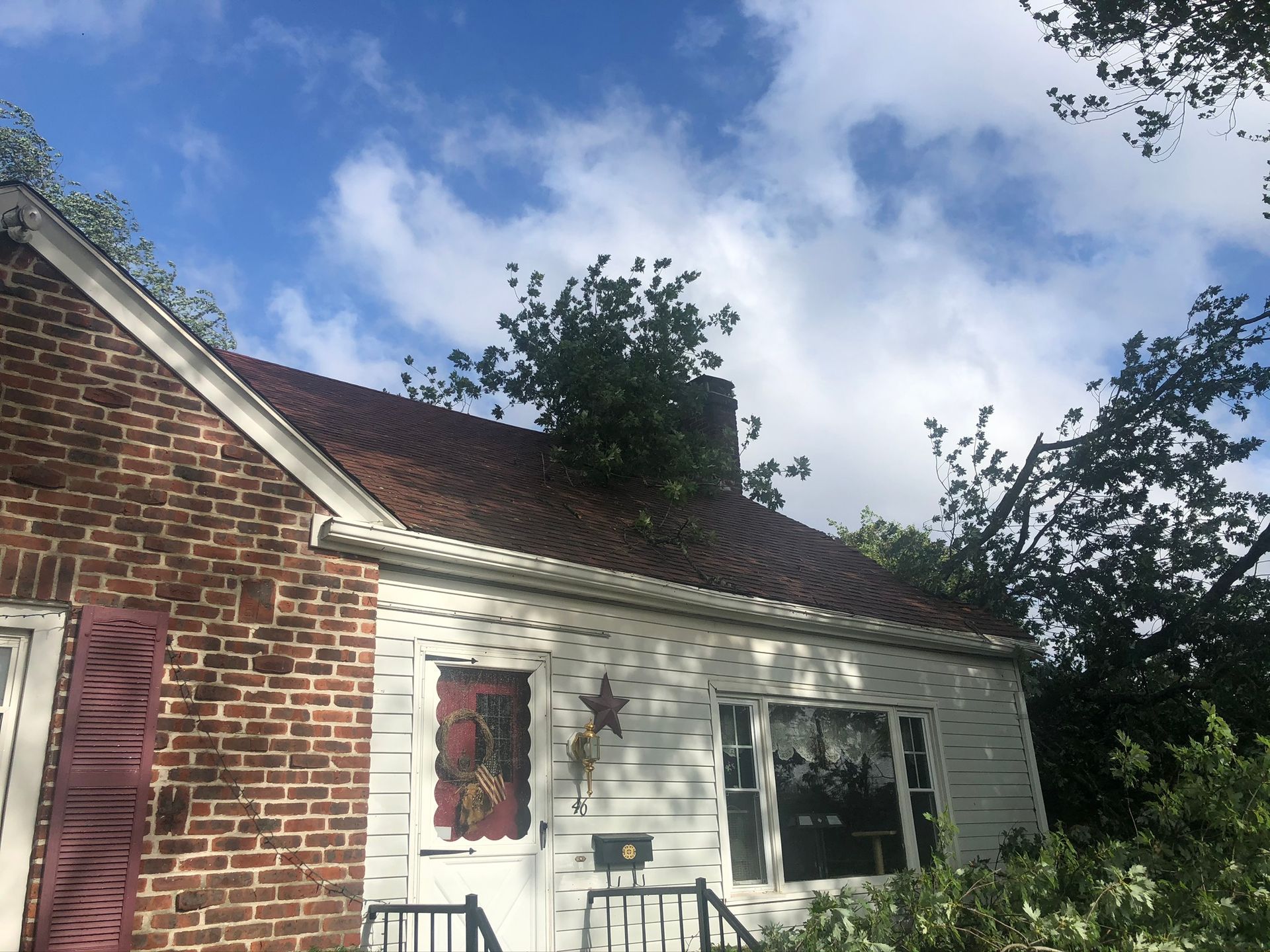 Brick house exterior with white siding, a window, and trees under a partly cloudy sky