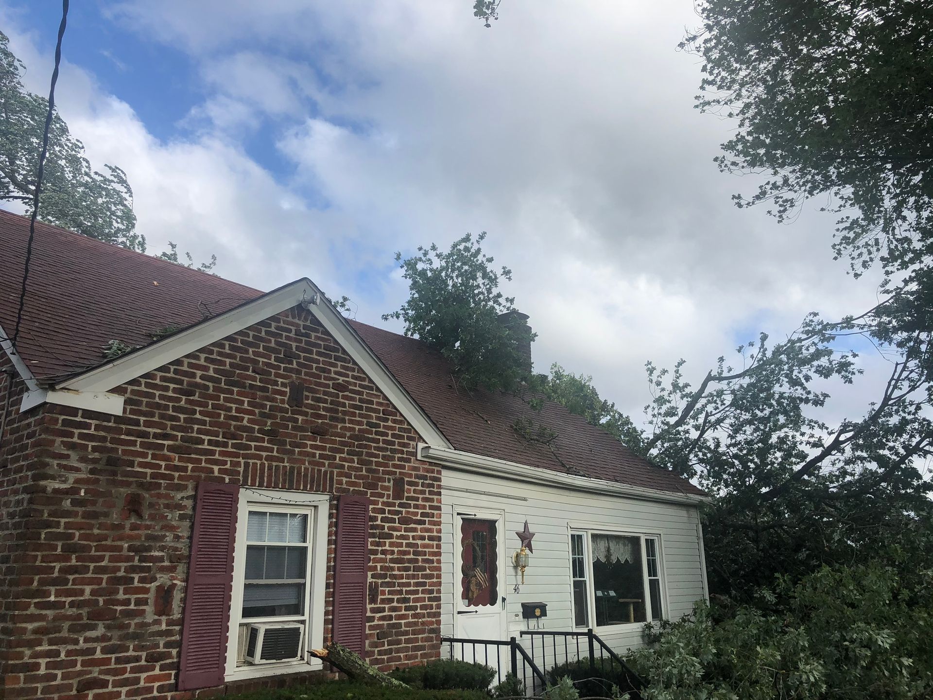 Brick house exterior with white siding, windows, and trees under a cloudy sky