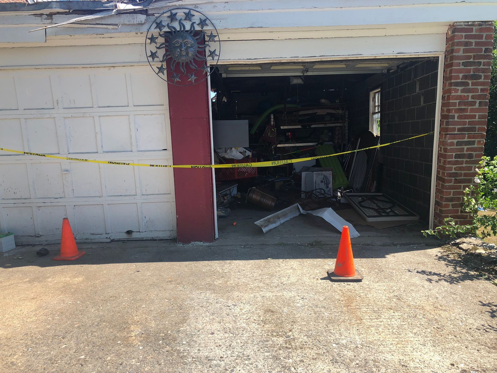 Garage with damaged open door, yellow caution tape, and orange cones blocking the entrance.
