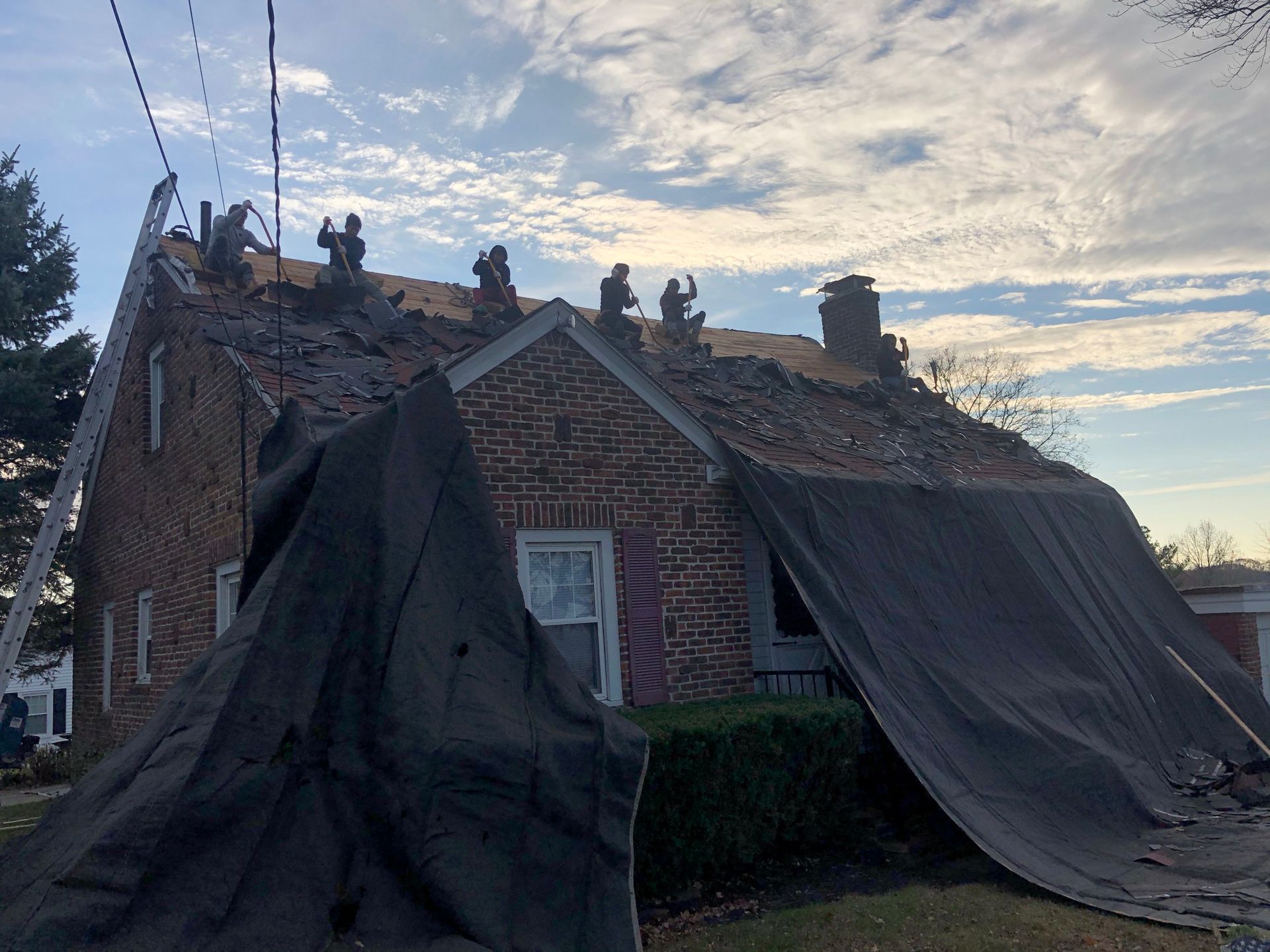 Damaged brick house with roof tarps and debris, seen at dusk after storm damage