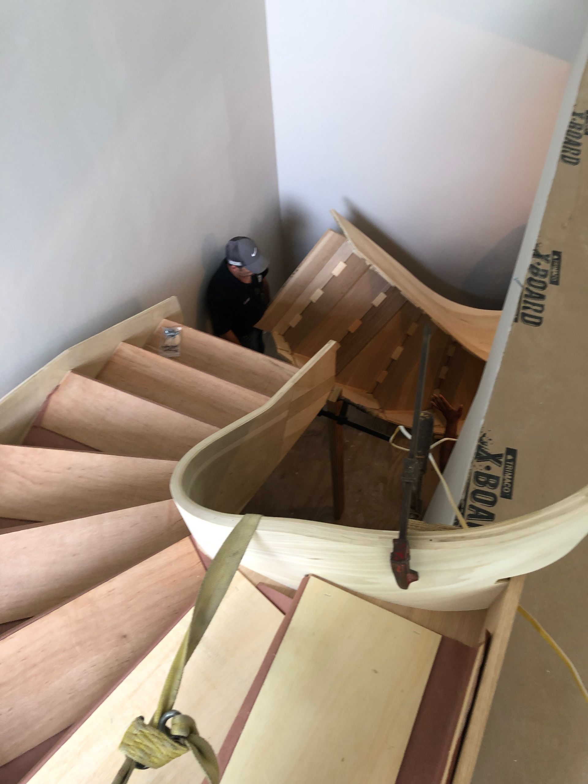Narrow spiral staircase under construction with unfinished wooden steps and a person working below