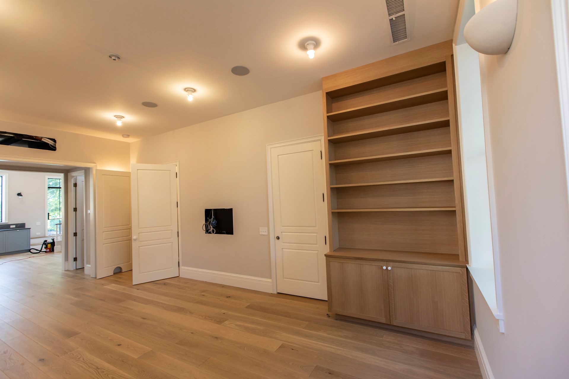 Bright modern empty room with wood floors, built-in shelving, recessed lights, and white doors