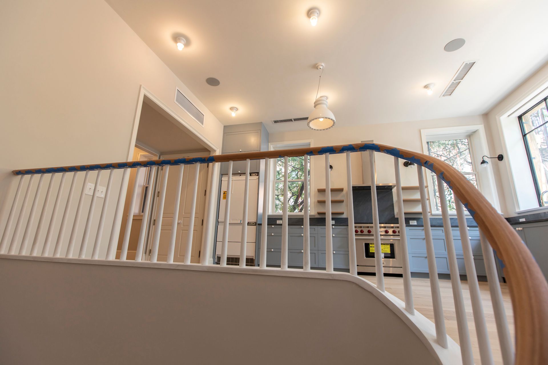 Bright modern interior with curved white railing, recessed lights, and kitchen in the background