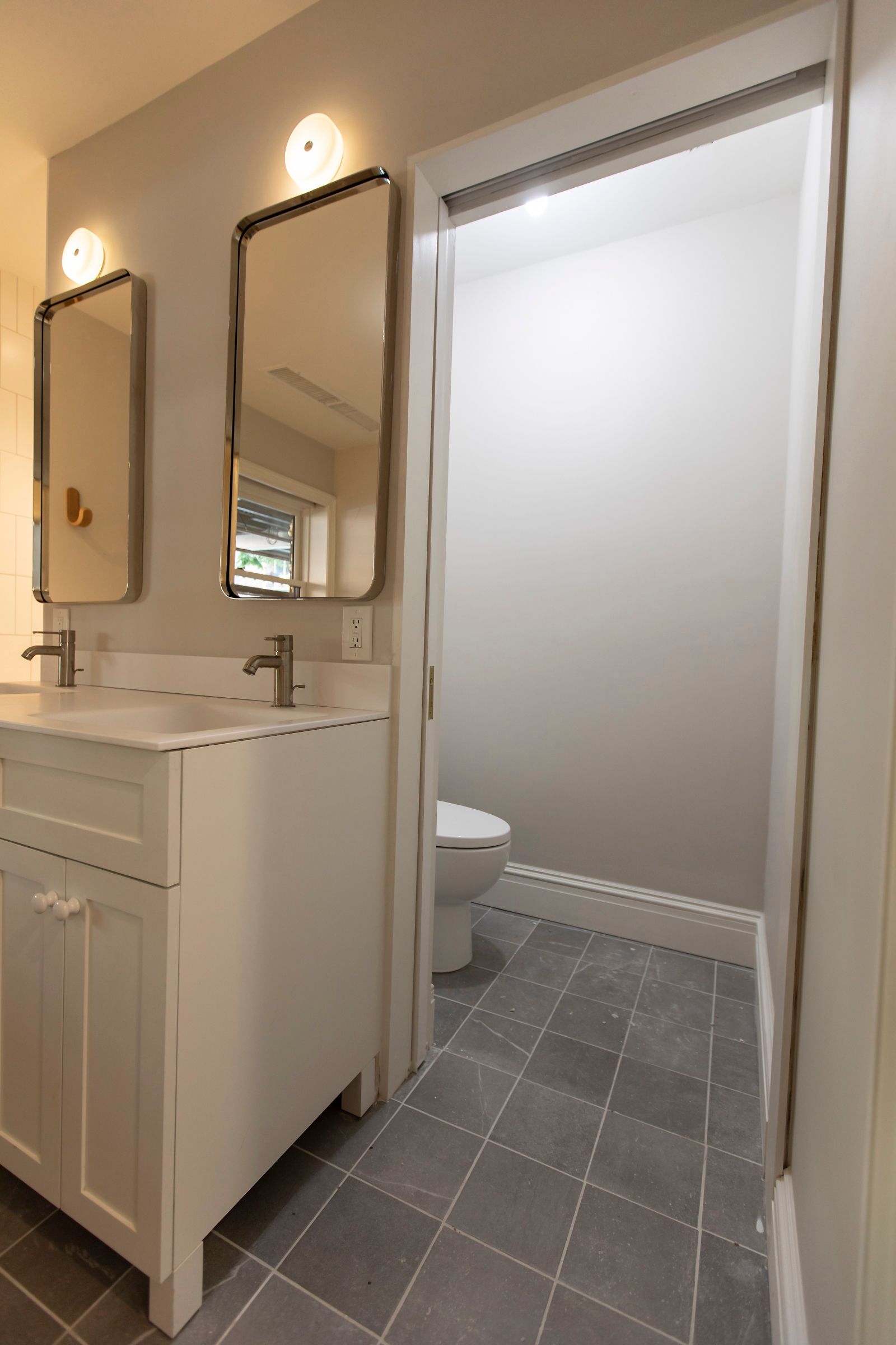 Small bathroom vanity with mirror, wall light, and toilet visible through a doorway
