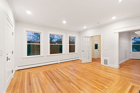 Empty, bright room with hardwood floors and multiple windows; doorway to other rooms.